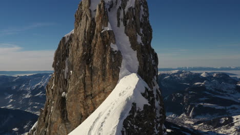 aerial video flying straight up viewing a rocky and snowy alpine peak in the french alps showing a large view behind in evening light