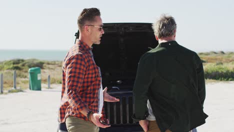 Estresada-Pareja-Masculina-Gay-Caucásico-De-Pie-Junto-A-Un-Coche-Averiado-Con-El-Capó-Abierto-En-La-Playa