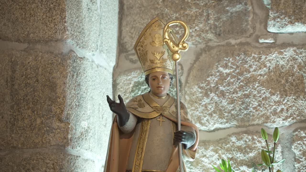 Primo piano di statua di santo vescovo cattolico con mitra e pastorale sullo sfondo di una parete interna in pietra di una chiesa
