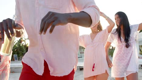 Happy-diverse-group-of-friends-dancing-holding-cocktails-at-beach