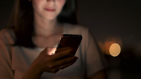 a young woman at night in the city calls a taxi through a smartphone while looking into the screen of a mobile phone and pointing out the coordinates and address of the trip.