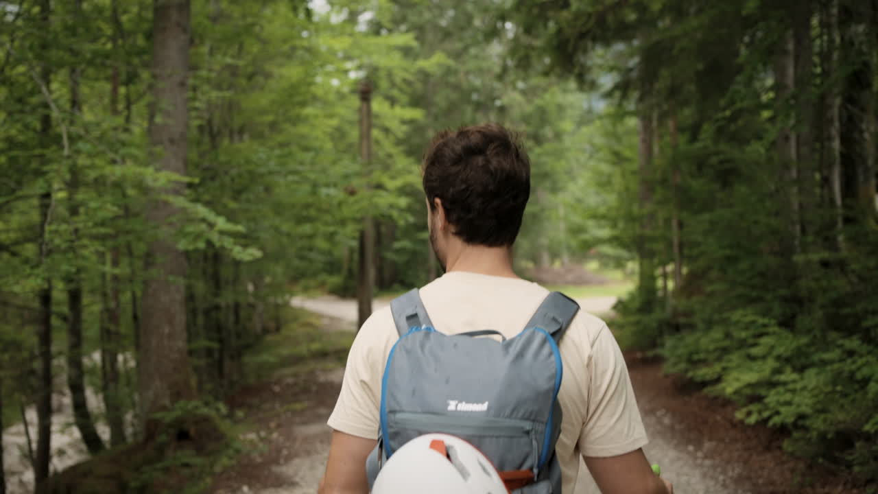 un joven caminando por un sendero en el bosque con la mochila gris y el casco blanco