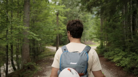 Ein-Junger-Mann,-Der-Mit-Grauem-Rucksack-Und-Weißem-Helm-Auf-Einem-Pfad-Im-Wald-Spaziert