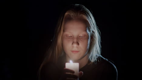 retrato de un niño mirando una vela ardiendo en la oscuridad