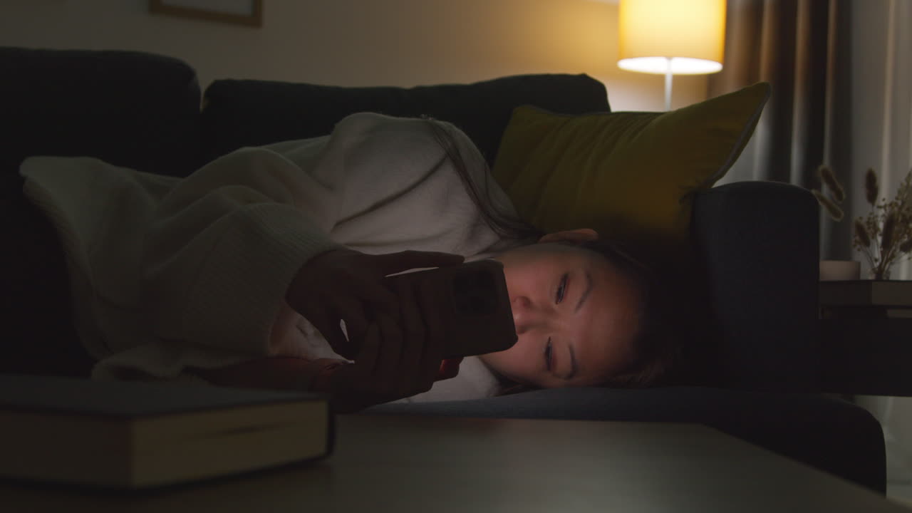 집에서 저녁을 보내고 소파에 누워 휴대전화를 들고 인터넷이나 소셜 미디어를 스크롤하는 여성 12