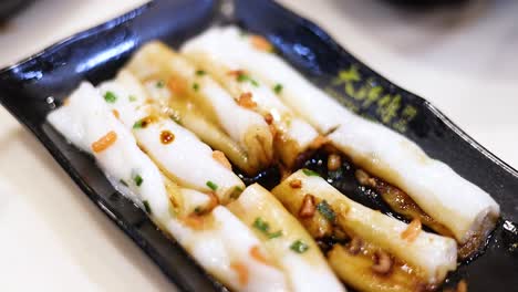 chopsticks lifting rice noodle rolls with sauce