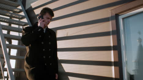 real estate manager in black coat descending staircase holding briefcase and talking on phone, as sunlight reflects onto building wall creating dynamic shadow