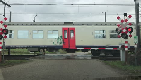 a passenger train crossing in font of a car on a rainy day