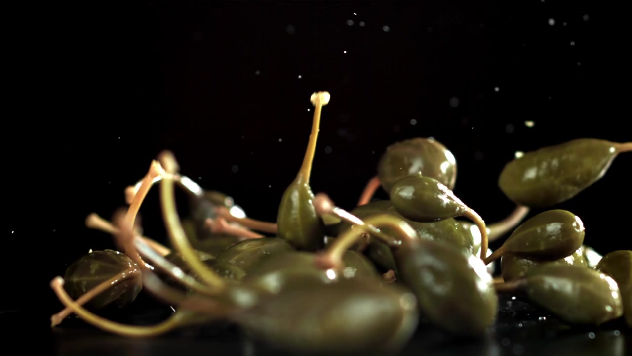 Färska kaprisbär som faller ner på en mörk yta i slow motion