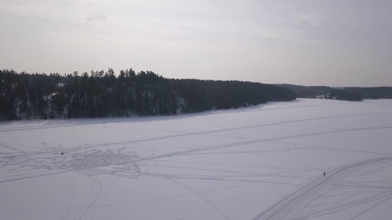 Аэросъемка, медленно панорамирующая вверх, чтобы показать бескрайность замерзшего озера посреди леса.