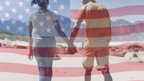 Animation-of-american-flag-moving-over-couple-holding-hands-and-walking-on-beach