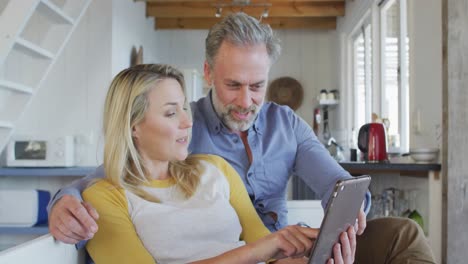 Glückliches-Kaukasisches-Reifes-Paar,-Das-Ein-Tablet-Benutzt-Und-Im-Wohnzimmer-Sitzt