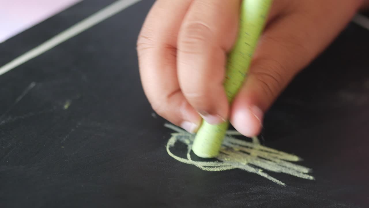 Closeup of a child's hand drawing on a chalkboard