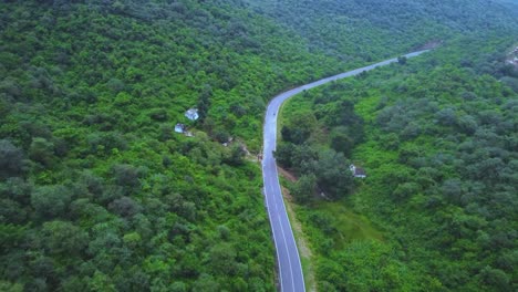 aerial drone view of a motor bike on forest road through lush green jungle with hilly backdrop during monsoon in gwalior madhya pradesh india