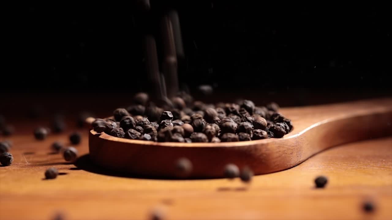 Black Tellicherry peppercorns closeup in wooden spoon on a kitchen table.