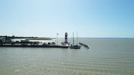 Aerial-drone-shot-of-a-lighthouse-with-a-pier-on-a-lake