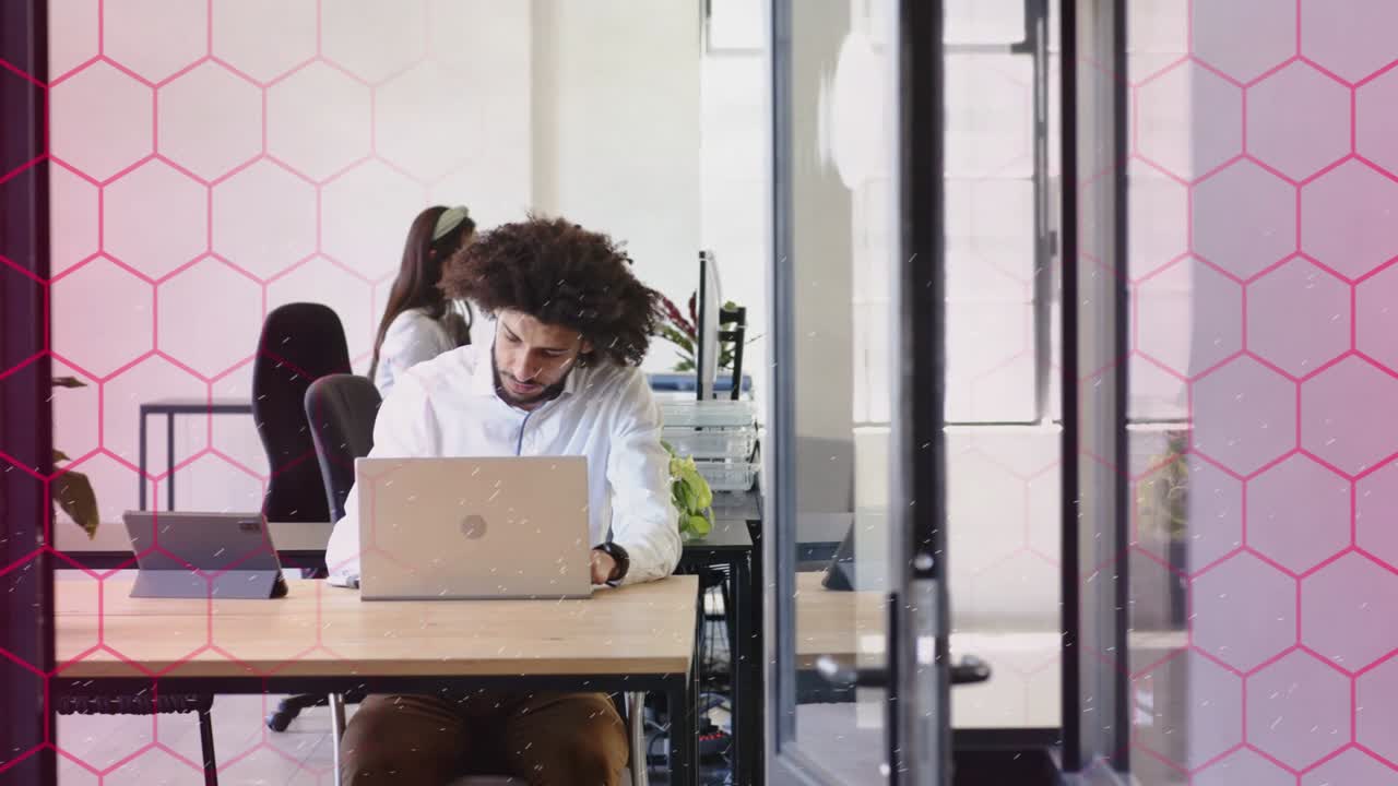 Trabajador masculino reaccionando al destello de la laptop y alcanzando un dispositivo tecnológico, mientras una superposición hexagonal rosa enmarca la laptop.