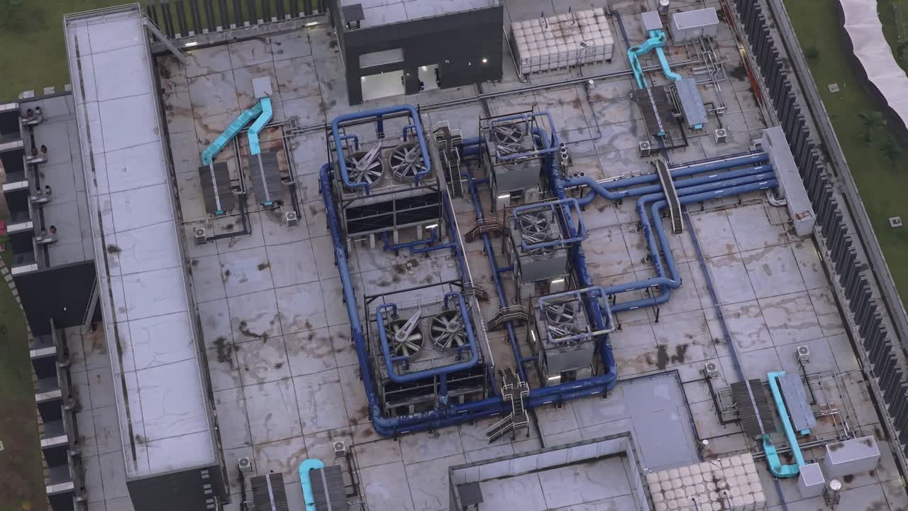 High angle aerial shot slowly rotating over a modern data center rooftop. Complex hvac systems, including cooling units and pipes, visible