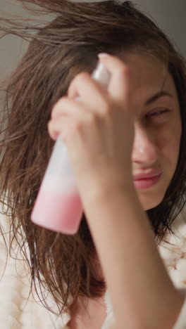 woman with short hair sprays cosmetic product closing eyes slow motion. female in plush light robe sprays care serum on hair in fancy bathroom