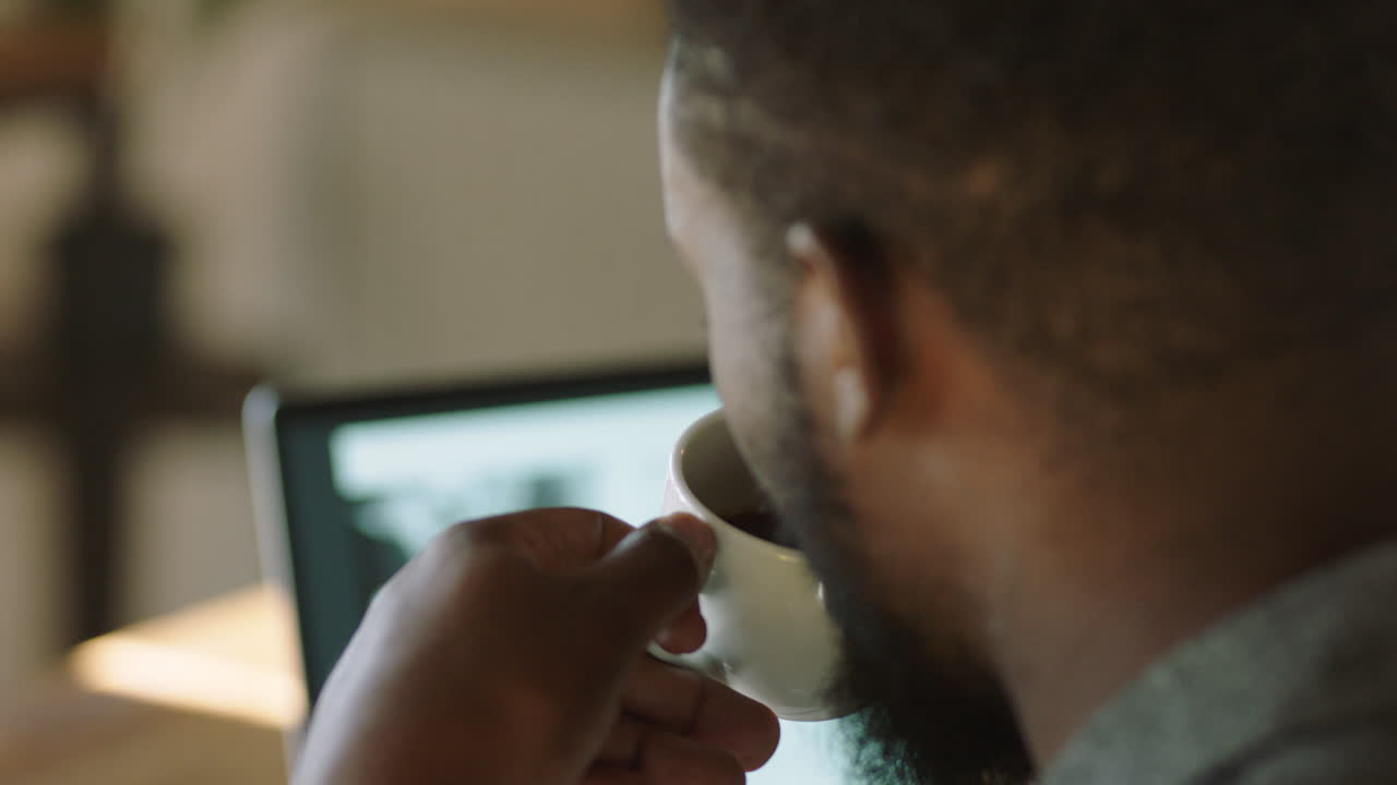 young african american businessman using laptop computer in cafe drinking coffee typing document working online sending email independent entrepreneur enjoying relaxed morning networking close up