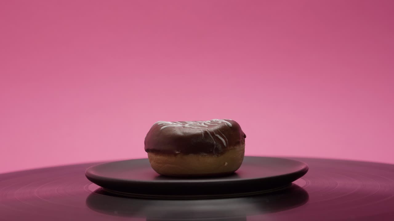 Delicious black chocolate donut rolls in a circle on a pink and black background