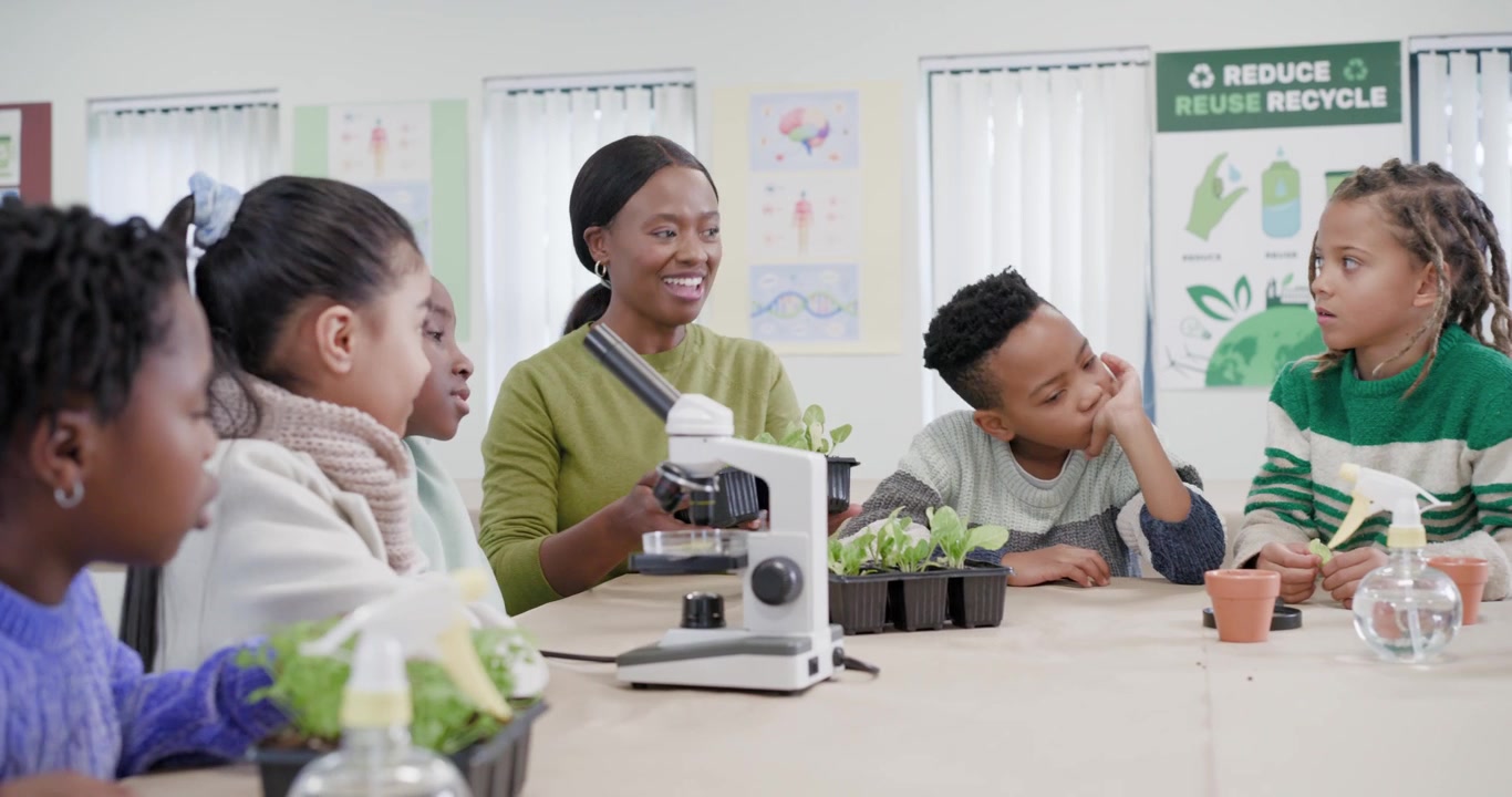 Female teacher presenting seedlings, guiding students to microscope for plant study at classroom
