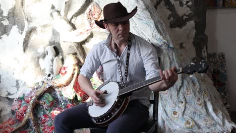 male musician playing banjo sitting chair indoor. video with sound.