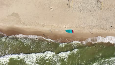 AERIAL:-Top-View-Shot-of-People-Walking-on-a-Beach-and-Surfers-Kite-Waving-in-Wind