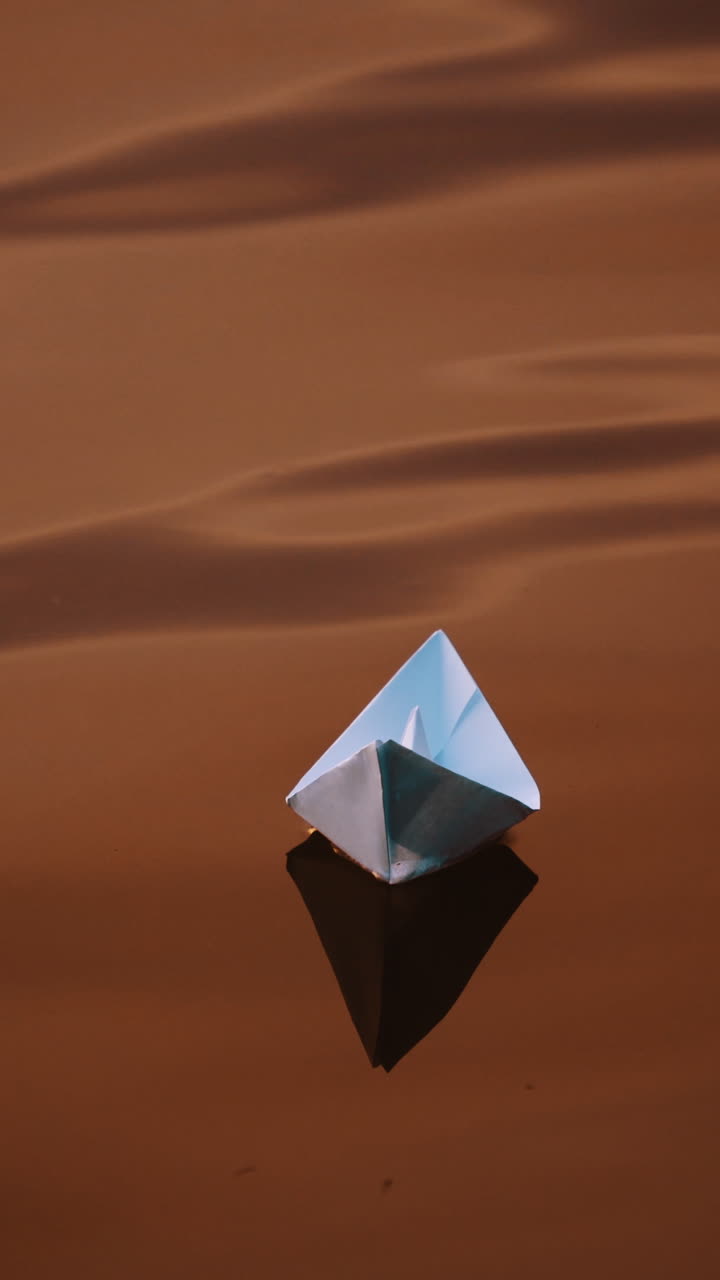 Dark background of water surface and paper ship floating in the evening. Homemade paper boat swimming outdoors at sunset. Vertical video