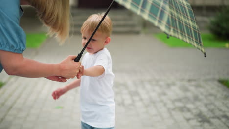 a little boy is seen trying to collect an umbrella from his mother, looking unhappy, with another child a little bit visible by the side