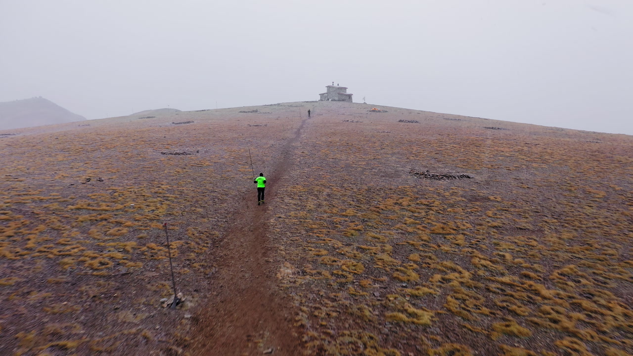 Hiker Walking on a Foggy Mountain Trail Towards a Distant Building