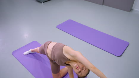 vista de arriba hacia abajo de una mujer realizando un estiramiento profundo en una alfombra de yoga púrpura, participando en entrenamiento de flexibilidad y equilibrio, postura relajada, respiración enfocada y alineación del cuerpo