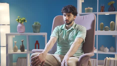 Stressed-young-man-sitting-alone-at-home-and-waving-his-feet-waiting-for-news-or-someone.