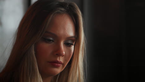 mujer joven sentada en una cafetería en una mesa de madera, bebiendo café y usando un teléfono inteligente. en la mesa hay una computadora portátil. chica navegando por internet, chateando, blogueando. mujer sosteniendo el teléfono y mirando su pantalla.