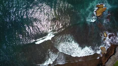 Top-view-of-Indian-Ocean-waves-breaking-over-coral-rock-reef-with-sun-reflection