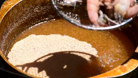 pot of bubbling hot oil deep frying seafood of shrimp in outdoor sunshine