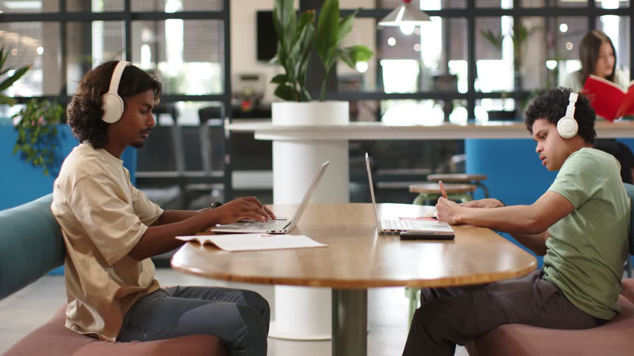 African American men opening laptops, typing and noting for study in coworking space with notebook