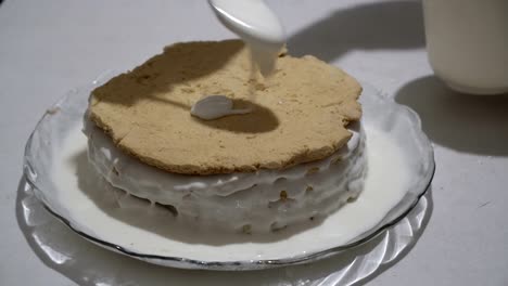 the female chef puts a new layer on the biscuit cake and smears it with cream on a glass plate. preparation of sweet dessert. close-up. the view from the top. 4k.