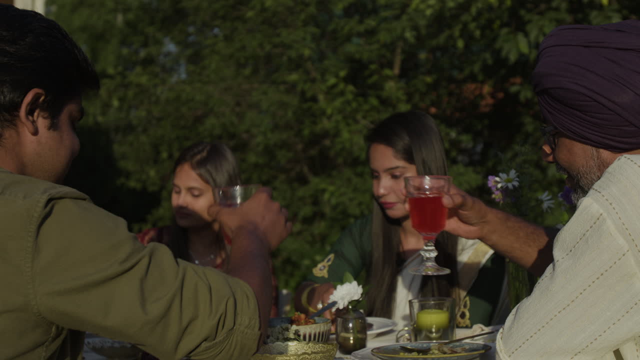 South Asian family or friends enjoying an outdoor meal with drinks in a garden setting