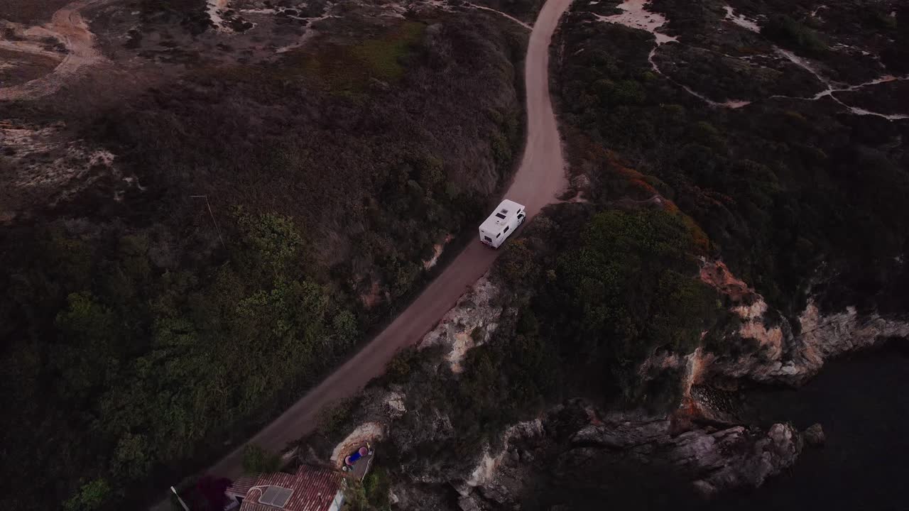 Portekiz'in Alentejo bölgesindeki Porto Covo yakınlarındaki Costa Vicentina Doğal Parkı içinde, Atlantik kıyısındaki şist kayalıklarına oyulmuş yükseltilmiş kıyı yolunda ilerleyen bir karavanın drone ile yukarıdan aşağıya (kuşbakışı) takibi.