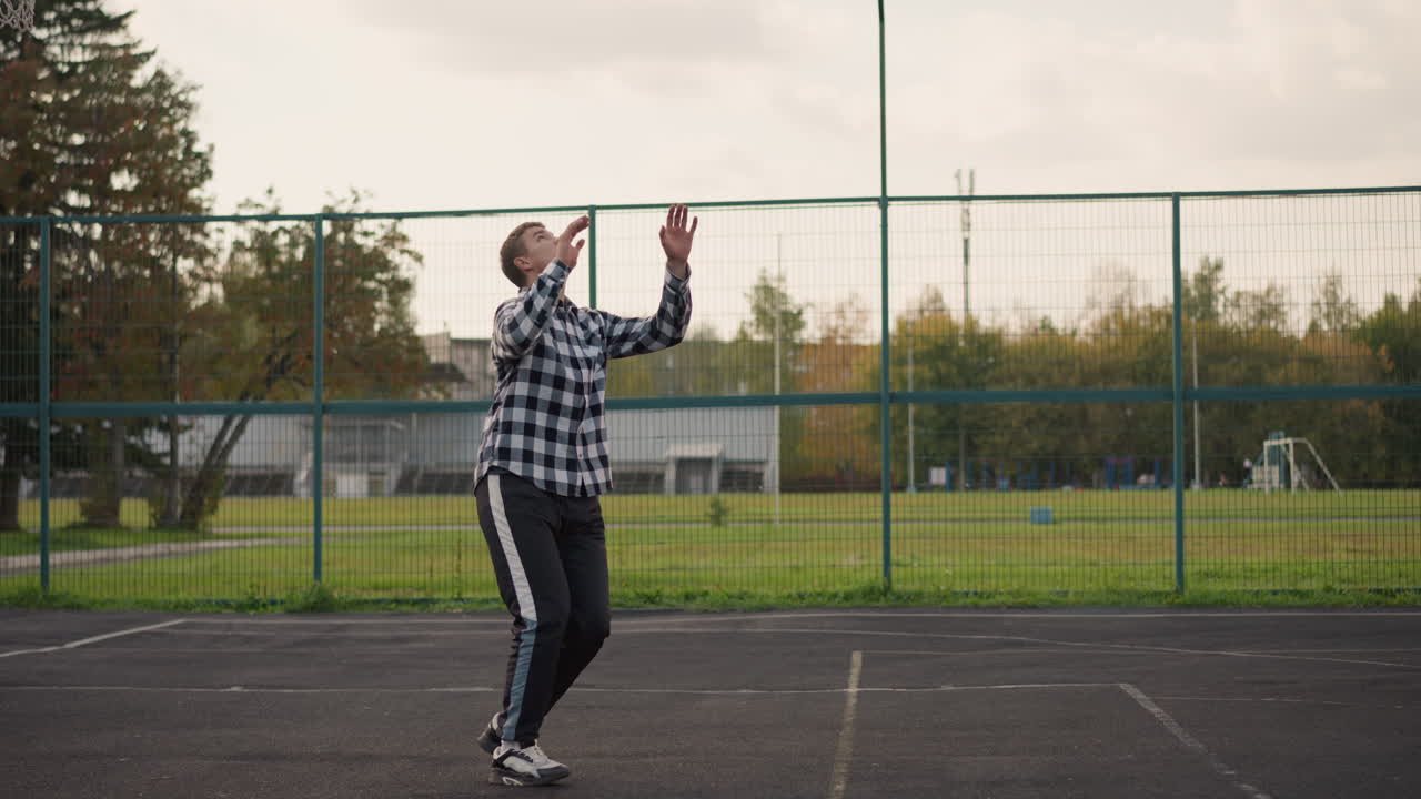 hombre en camisa a cuadros en la cancha al aire libre lanzando voleibol hacia arriba, preparándose para atacar con el fondo mostrando campo verde y equipos deportivos, acción deportiva intensa y atletismo