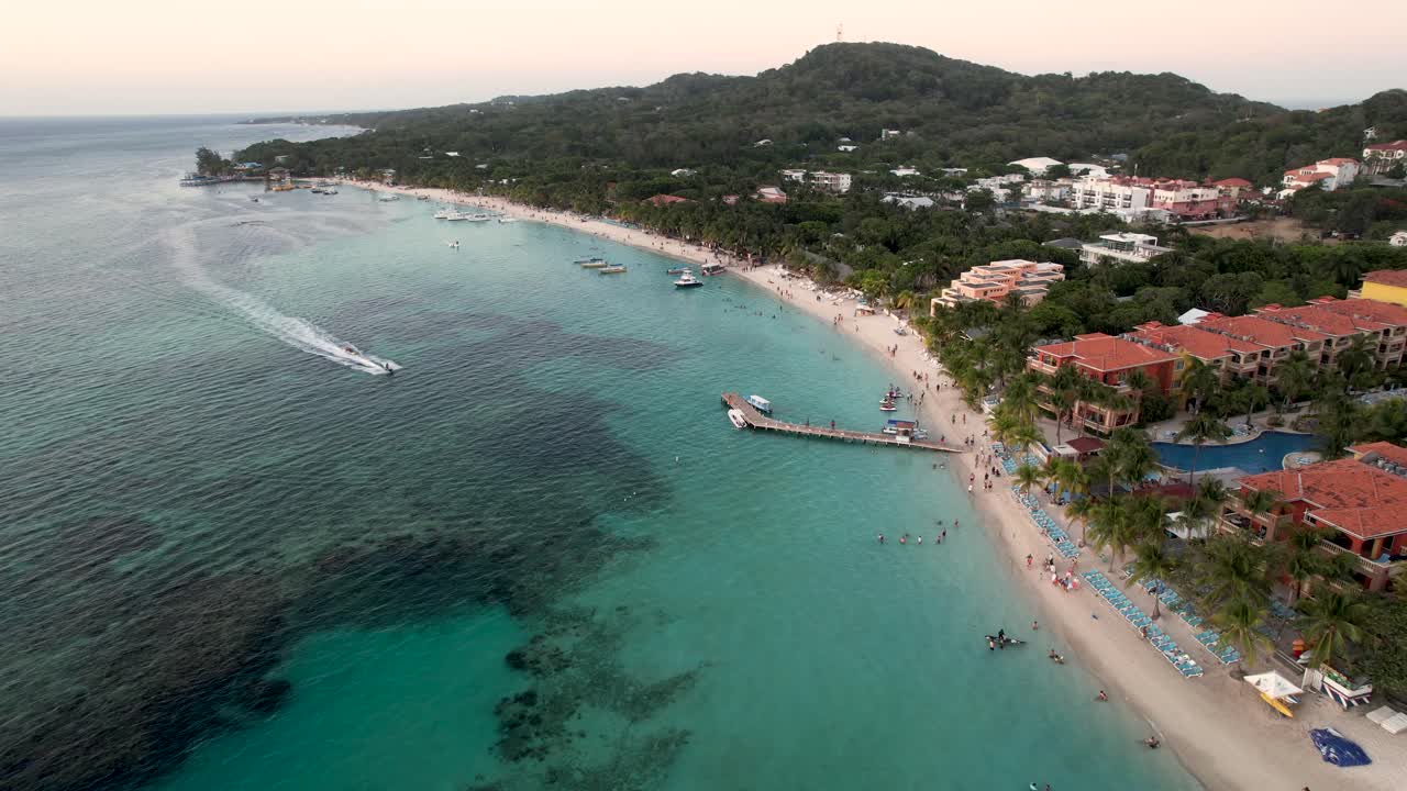 Vista aerea della costa, motoscafi, banana boat, palme verdi sulla spiaggia sabbiosa al tramonto.