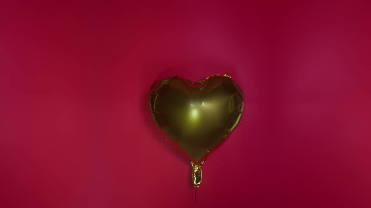 Globo dorado en forma de corazón balanceándose sobre un fondo rojo