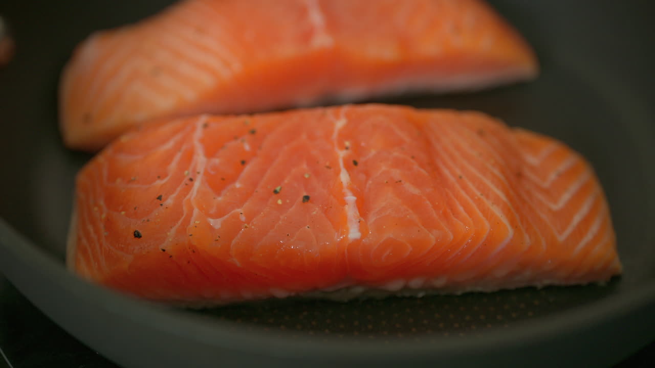 Close up of red salmon seasoned with salt and black pepper cooking on a pan