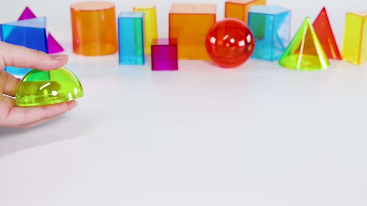 Vibrant 3D geometric shapes interact on a white surface, highlighting movement and color contrast in a playful educational setting