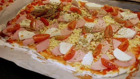 la cocinera casera está vertiendo especias frescas en pizza casera con mozzarella y tomates