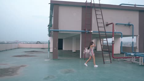 짧은 드레스 스니커 를 입은 여자 가 호텔 지붕 에 있는 사다리 를 올라간다