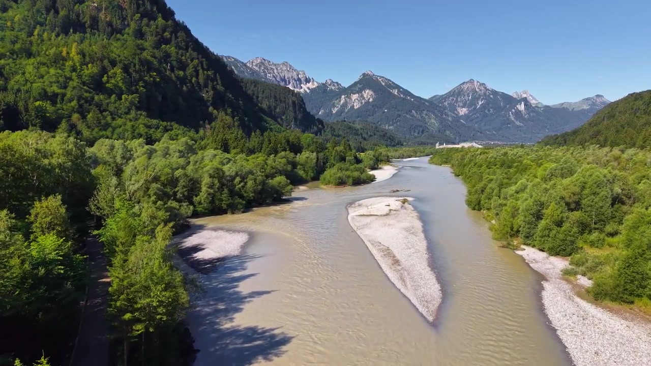 Vista aerea con drone del fiume Lech con ampie rive ghiaiose che attraversa una foresta verde verso le Alpi, Füssen, Germania