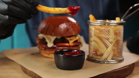 hand dipping french fries in ketchup with burger and fries on a plate