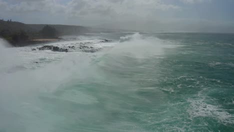 Vista-Aérea-De-Las-Enormes-Olas-Del-Océano-Pacífico-Rompiendo-Contra-Las-Rocas-De-Coral-Y-Salpicando-En-El-Aire-De-La-Costa-Norte-Cerca-De-Sharks-Cove-Hawaii